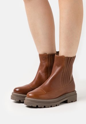 Braune Leder-Ankelboots mit gerippten Seiten, runder Schuhspitze und dicker Gummisohle. Glatte Textur mit sichtbaren Nähdetails.