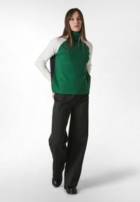 Zelený, bílý a černý turtleneck svetr s dlouhými rukávy, v kombinaci s černými širokými kalhotami s proužky a černými botami.