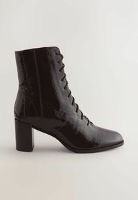 Fekete lakkbőr bokacsizma, fűzős elejével, hegyes orral és tömzsi sarokkal. Simára kidolgozott felület elegáns fényességgel.