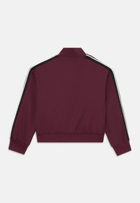 Burgundi sportdzseki magas gallérral, fekete és fehér oldalsávokkal és bordás mandzsettákkal. Simább anyagból készült és cropped fazonú.