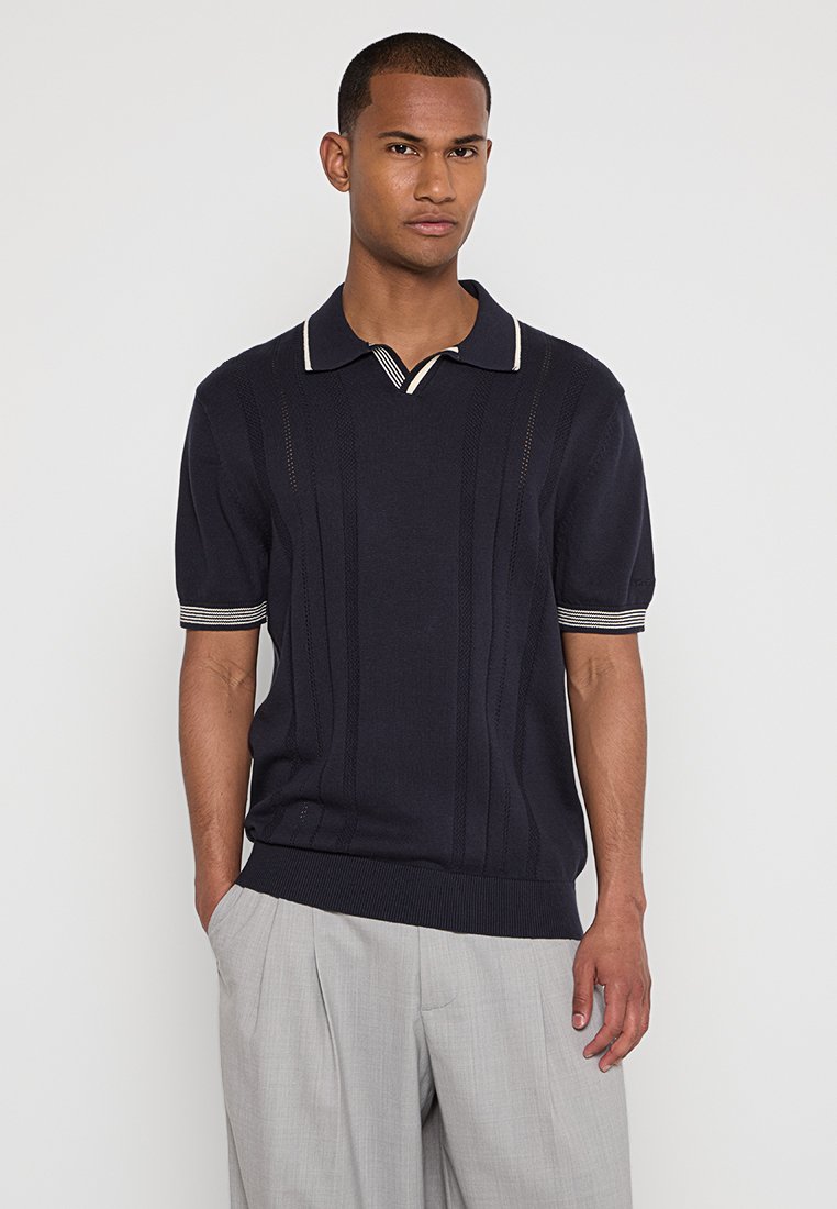 Polo à manches courtes bleu marine avec texture côtelée verticale, col et poignets rayés contrastants, coupe ajustée et tissu en maille douce.