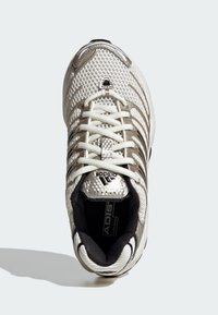 Biały but sportowy z siateczkową cholewką, gumową podeszwą i kontrastowymi czarnymi akcentami. Posiada system sznurowania i fakturowane detale po bokach.