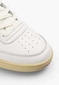 Zapatilla blanca de cuero con caja de dedos perforada, suela de goma beige texturizada y cordones de algodón planos. Acabado liso con detalles de costura sutil.