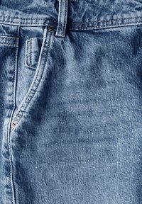 Světle modré denimové džíny s detailním pohledem na textura látky, s uzávěrem na knoflík a poutkem na opasek.