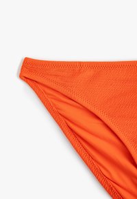 Parte inferiore di bikini arancione realizzata in tessuto testurizzato. Presenta una cucitura liscia lungo i bordi e un design a vita bassa.