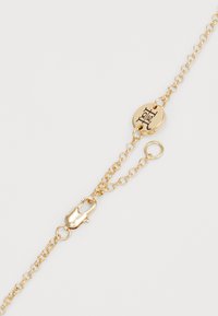 Bracelet en chaîne dorée avec un fermoir rond, équipé d'un charm décoratif rond gravé. Les maillons sont de taille uniforme, créant un aspect délicat.