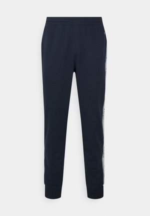 Marineblaue, zulaufende Jogginghose mit elastischem Bund und gerippten Bündchen, mit einem weißen Streifen mit schwarzem Text an den Außenseiten.
