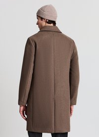 Cappotto marrone di lana con taglio dritto, colletto a revers e maniche lunghe. Indossato sopra un outfit grigio, con un berretto lavorato a maglia di colore chiaro.