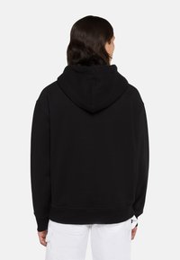 Sudadera negra con capucha grande, corte holgado, tela suave y puños y dobladillo acanalados. La parte trasera es lisa, sin detalles adicionales.