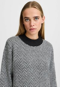 Schwarz-weißer Pullover mit Fischgrätmuster und geripptem schwarzen Kragen. Weicher Stoff, leicht lockere Passform, Rundhalsausschnitt.