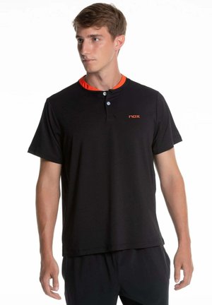 Junger Mann trägt ein schwarzes Henley-Shirt mit kurzen Ärmeln und "nox"-Logo, schaut nach links vor weißem Hintergrund.