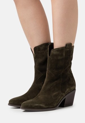 Donkergroene suèdé enkellaarsjes met een puntige neus, decoratieve stiksels en een lage blokhak. Voorzien van zijritsen en uitwijkaccenten.