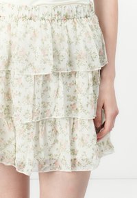 Gonna a balze floreale in tessuto leggero e trasparente con motivi di fiori rosa e verdi. Presenta una morbida vita elastica per il comfort.