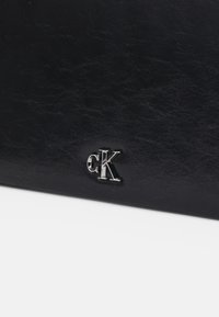 Black faux leather wallet featuring a textured surface, embossed silver "cK" logo, and a sleek rectangular shape.