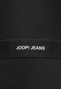 Schwarzer Stoff mit mittig platziertem schwarzem Band, das weißen Text "JOOP! JEANS" in Großbuchstaben zeigt.