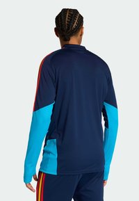 Camisola desportiva azul-marinho de manga comprida com realces turquesa e riscas vermelhas. Apresenta uma gola alta e painéis texturizados nas mangas.