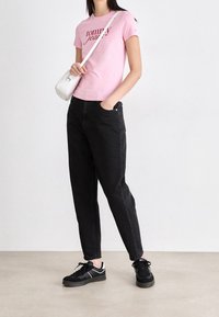 Camisa rosa de manga corta con texto "Tommy", jeans negros ajustados y zapatillas negras. Accesorio: bolso cruzado pequeño blanco.