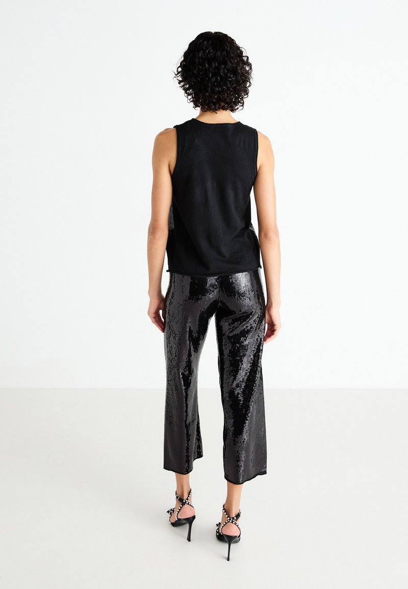 Schwarzes ärmelloses Top, kombiniert mit glänzenden schwarzen Pailletten-Culottes. Die Schuhe umfassen hochhackige Sandalen mit Riemen und dekorativen Akzenten.