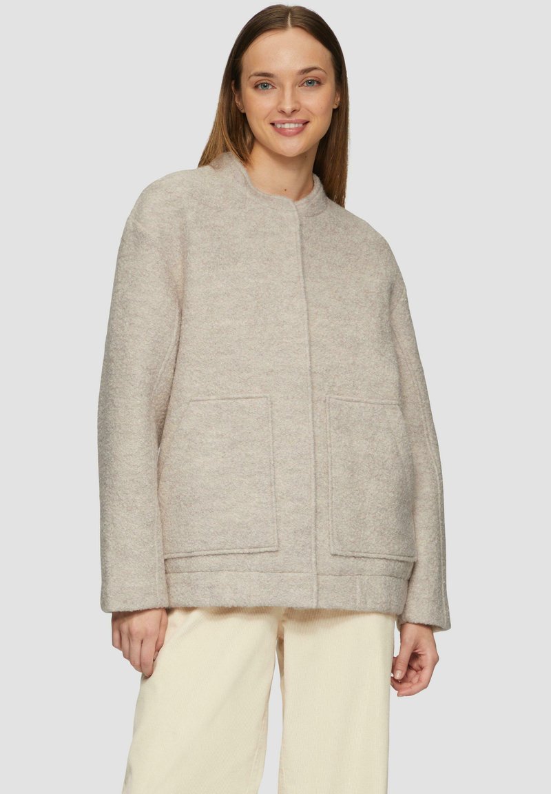 Beige wolmix jas met een ronde halslijn, twee voorzakken en een relaxte pasvorm. Soepele textuur en minimalistisch ontwerp.