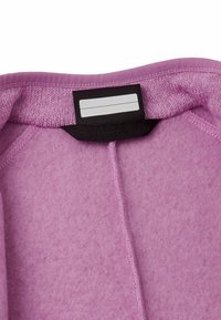 Wnętrze fioletowego polaru z czarną metką. Charakteryzuje się miękką teksturą, starannym przeszyciem i schludnym dekoltem.