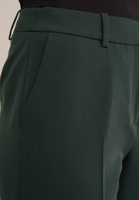 Mörkgröna skräddarsydda byxor med en mjuk textur, som har en slät framsida, sidofickor och en subtil glans på tyget.