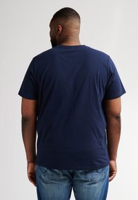 Tmavě modré tričko s krátkým rukávem a kulatým výstřihem, vyrobené z měkké bavlny, kombinované se světle modrými džíny, což vytváří uvolněný vzhled.