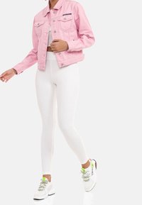 Rosa denimjacka med silverknappar, två bröstfickor, i kombination med vita ribbade leggings och flerfärgade sneakers med neonlysande accenter.