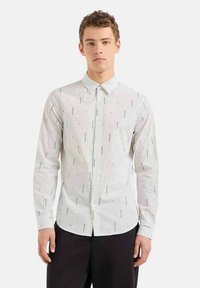 Camicia bianca con bottoni, caratterizzata da strisce verticali nere e linee nere di accento sparse. Maniche lunghe, colletto standard, design slim fit.