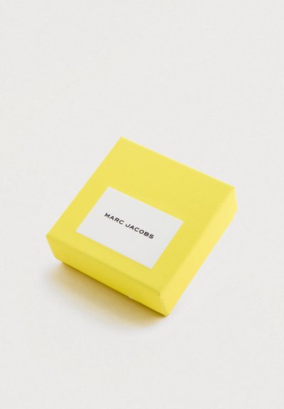 Caja de embalaje cuadrada amarilla con una textura suave, que presenta una etiqueta blanca con texto negro que dice "MARC JACOBS."