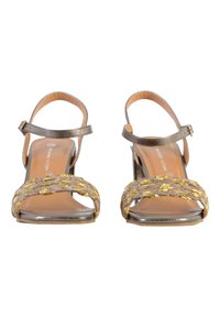 Sandalias metálicas plateadas con una correa trenzada de oro y beige, diseño de punta abierta, hebilla ajustable en el tobillo y una base beige suave.