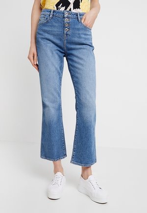 Lichtblauwe denim jeans met een hoge taille, sluiting met vijf knopen, voorzakken en een uitlopende zoom. Gecombineerd met witte platformsneakers.