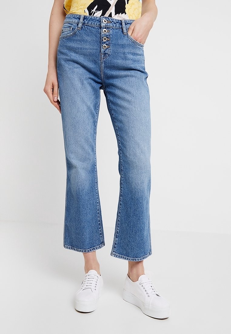 Lichtblauwe denim jeans met een hoge taille, sluiting met vijf knopen, voorzakken en een uitlopende zoom. Gecombineerd met witte platformsneakers.