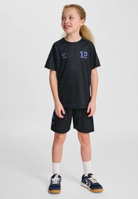 Zwarte sportoutfit met een shirt met korte mouwen met paarse accenten en het nummer 12, gecombineerd met bijpassende shorts. Sneakers met witte veters.
