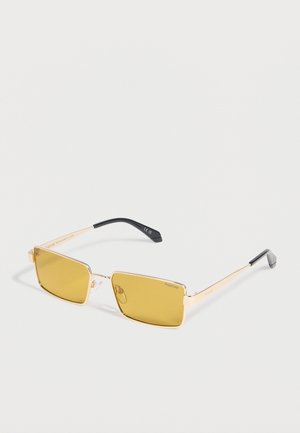 Rektangulære solbriller med guldfarvede stel og gule, tonede linser samt sorte stangender, vist på en hvid baggrund.
