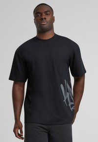 Black short-sleeve t-shirt made of cotton, featuring a large gray graphic design on the left side; round neckline and relaxed fit.