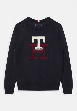 Granatowy sweter z dzianiny z dużymi białymi i czerwonymi literami "TH" oraz małą metką "Tommy" na środku klatki piersiowej, z prążkowanymi mankietami i dołem.