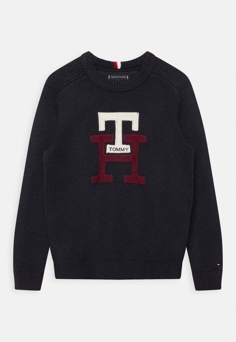 Pull en tricot bleu marine avec de grandes lettres blanches et rouges "TH" et une petite étiquette "Tommy" centrée sur la poitrine, poignets et ourlet côtelés.