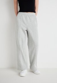 Graue Sweatpants mit weitem Bein, elastischem Bund und Nahtdetails. Kombiniert mit weißen Sneakers und einem schwarzen, verkürzten Oberteil.