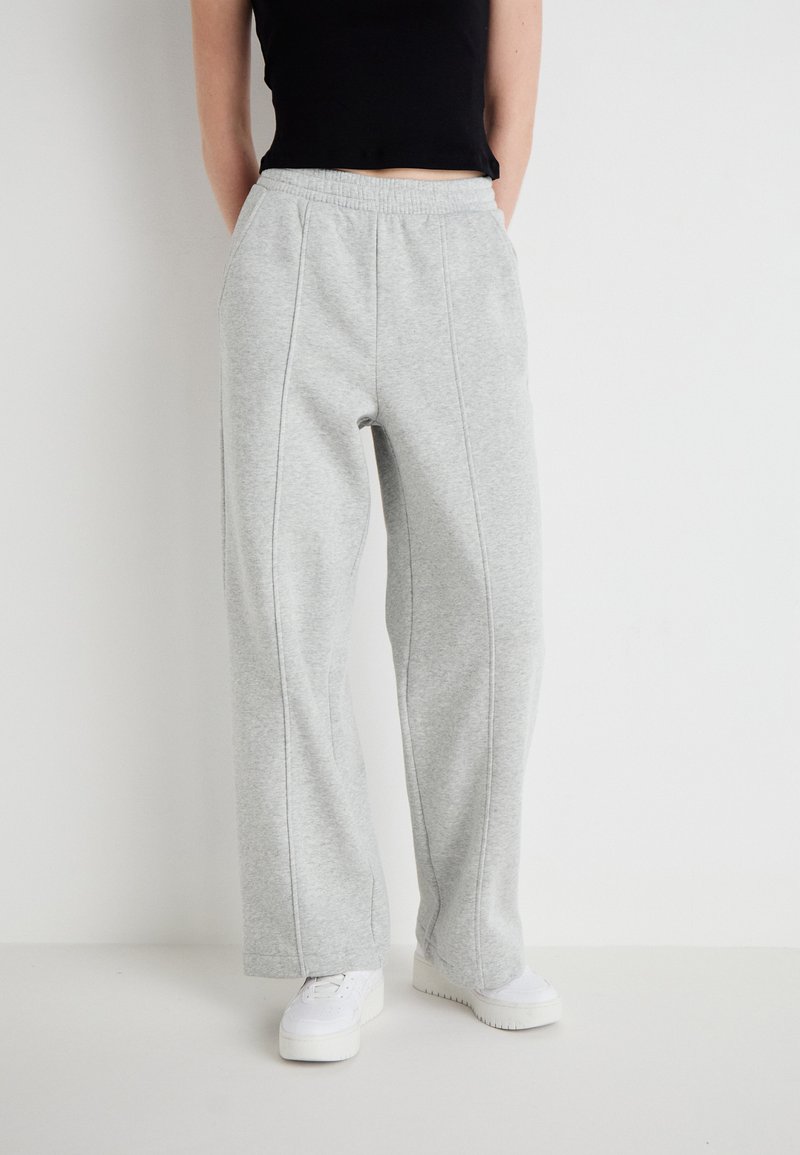 Graue Sweatpants mit weitem Bein, elastischem Bund und Nahtdetails. Kombiniert mit weißen Sneakers und einem schwarzen, verkürzten Oberteil.