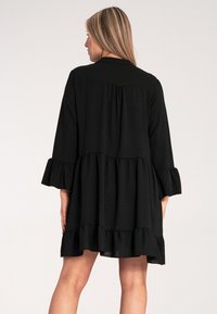 Czarna sukienka o warstwowym fasonie, z falbaniastymi rękawami i kołnierzykiem. Wykonana z fakturowanej tkaniny, sięga nieco powyżej kolan.
