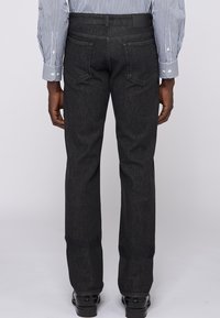 Pantalones de mezclilla gris oscuro vistos desde atrás, con un corte de pierna recta, dos bolsillos traseros y una etiqueta en la cinturilla.