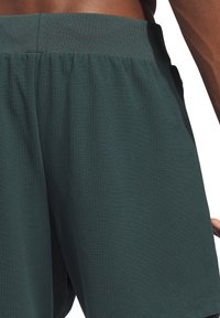 Donkergroene sportshorts met een gestructureerd oppervlak. Voorzien van een elastische tailleband en een zijzak, ontworpen voor comfort en functionaliteit.