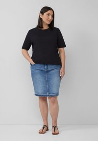 Schwarzes kurzärmliges T-Shirt, kombiniert mit einem hellblauen Jeans-Bleistiftrock. Der Rock hat einen fransigen Saum und das Modell trägt schwarze Flip-Flops.