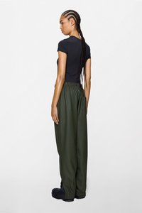 Čierne priliehavé tričko v kombinácii s voľnými tmavozelenými nohavicami z elastickým pásom a nariasenými manžetami, nosené s čiernymi topánkami.