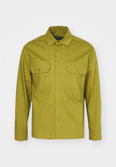 Dolga majica z dolgimi rokavi v olivno zeleni barvi, izdelana s kombinacijo bombaža, z ovratnikom na gumbe in dvema sprednjima žepoma s pokrovčkom na gumbe.