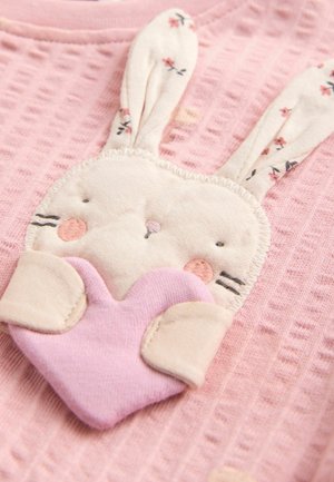 Rosa Stoffhemd mit einem Hasendesign, das gestickte Details, lange Ohren und ein Herz aufweist. Weicher Stoff und verspielte Blumenakzente.