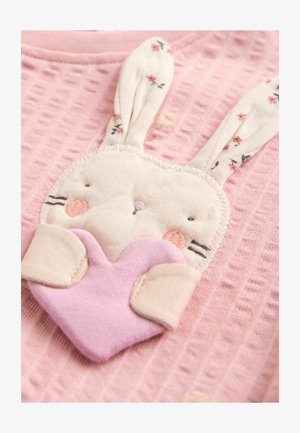 Roza tkaninska srajca z načrtom zajca, ki vključuje vezenine, dolge uhlje in srce. Mehka tekstura in igrivi cvetlični poudarki.