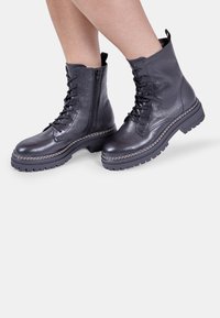 Botine negre din piele cu șireturi pe partea din față, închidere cu fermoar și finisaj texturat. Talpă din cauciuc cu detalii contrastante de cusătură.