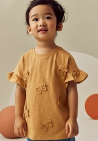 Senfgelbes T-Shirt mit kurzen Ärmeln und Rüsche an den Bündchen, verziert mit gestickten Schmetterlingsmotiven. Entworfen mit einer lockeren Passform und weichem Material.