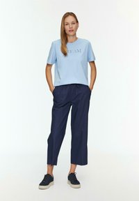Jasnoniebieska bawełniana koszulka z napisem "DREAM"; zestawiona z granatowymi, luźnymi spodniami 3/4; czarne trampki z kremowymi podeszwami.